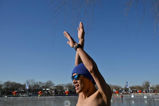 Zhang Xin, a winter swimming enthusiast warms up before swimming at the Houhai Lake of the Shichahai scenic area in Beijing on January 20, 2026. Every winter dozens of locals add to their daily routine a frigid lap in the icy waters of Shichahai, a sprawling lake in the center of the Chinese capital. (Photo by Adek BERRY / AFP)