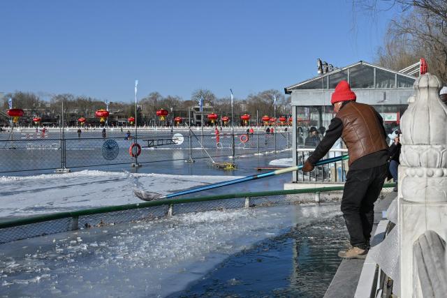 A man cleans ice as winter swimming enthusiasts swim at the Houhai Lake of the Shichahai scenic area in Beijing on January 20, 2026. Every winter dozens of locals add to their daily routine a frigid lap in the icy waters of Shichahai, a sprawling lake in the center of the Chinese capital. (Photo by Adek BERRY / AFP)