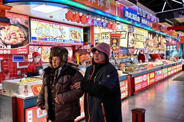 People walk next to stands selling food at the Huangpu district in Shanghai on January 20, 2026. (Photo by Hector RETAMAL / AFP)
