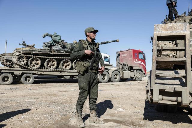 A member of the Syrian government forces stands next to tanks loaded on trucks along a road in the area of Khirbat At Tamr, south of the city of Hasakeh in northeastern Syria, on January 20, 2026, as they head towards the city. Negotiations have collapsed between the Syrian president and the chief of the country's Kurdish-led forces, a Kurdish official told AFP, as the army deployed reinforcements to flashpoint areas in the north. (Photo by Bakr ALkasem / AFP)