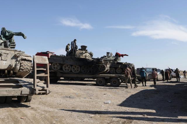 Syrian government forces stand on a tank loaded on a truck along a road in the area of Khirbat At Tamr, south of the city of Hasakeh in northeastern Syria, on January 20, 2026, as they head towards the city. Negotiations have collapsed between the Syrian president and the chief of the country's Kurdish-led forces, a Kurdish official told AFP, as the army deployed reinforcements to flashpoint areas in the north. (Photo by Bakr ALkasem / AFP)