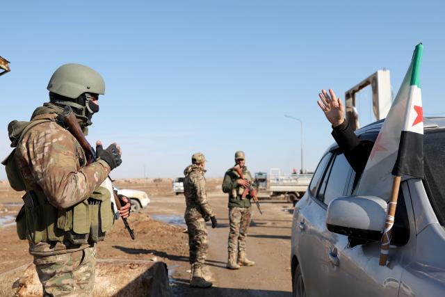 A residents waves as Syrian government forces man a checkpoint after entering the city of Ash Shaddadah south of the city of Hasakeh in northeastern Syria on January 20, 2026. Negotiations between Syria's President and the head of the Kurdish-led Syrian Democratic Forces, have collapsed, a Kurdish official told AFP January 20. It came after rapid army gains in Kurdish-controlled territory, with the president refusing to concede on a push for decentralisation even while pledging to protect the minority's rights. (Photo by OMAR HAJ KADOUR / AFP)