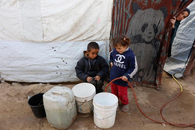 Children fill buckets with water outside their tent in Gaza City on January 20, 2026. Day-to-day living conditions for the vast majority of Gaza residents remain extremely precarious, with more than 80 percent of infrastructure destroyed, according to the United Nations. Several humanitarian and UN workers told AFP that while the situation has improved in some areas since the ceasefire, the humanitarian response remains insufficient due to access restrictions imposed by Israeli authorities -- who deny these claims. Water and electricity networks, as well as waste management, no longer function. (Photo by Omar AL-QATTAA / AFP)