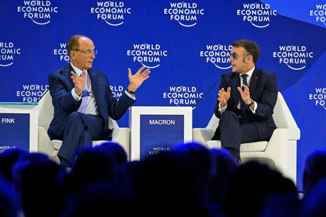 France's President Emmanuel Macron (R) gestures as he speaks next to BlackRock chairman and WEF co-chairman Larry Fink during the World Economic Forum (WEF) annual meeting in Davos on January 20, 2026. The World Economic Forum takes place in Davos from January 19 to January 23, 2026. (Photo by Fabrice COFFRINI / AFP)