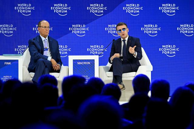 France's President Emmanuel Macron (R) gestures as he speaks next to BlackRock chairman and WEF co-chairman Larry Fink during the World Economic Forum (WEF) annual meeting in Davos on January 20, 2026. The World Economic Forum takes place in Davos from January 19 to January 23, 2026. (Photo by Fabrice COFFRINI / AFP)