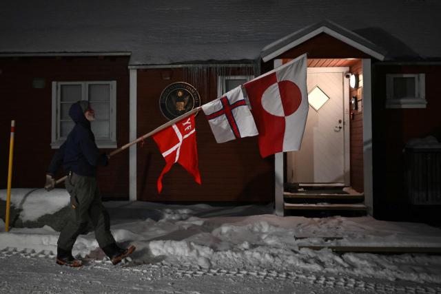 Jens Kjeldsen, a 70-year-old carpenter and former judge from Greenland, paces with flags of Denmark, the Faroe Islands and Greenland (Kingdom of Denmark) protesting outside the US consulate's wooden cabin in Nuuk, Greenland, on January 20, 2026. The 70-year-old carpenter and former judge from Greenland is holding daily early morning protests outside the US consulate this week in hopes of getting his message across to US officials. (Photo by Jonathan Nackstrand / AFP)