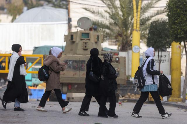 Women walk past an Israeli armoured vehicle after Israel's security forces closed part of the H2 southern sector of the occupied West Bank city of Hebron, and announced a curfew as they search for weapons and Palestinians on their wanted list, on January 20, 2026. Following the 1995 Oslo Agreement and subsequent 1997 Hebron Agreement, Palestinian cities in the West Bank were placed under the exclusive jurisdiction of the Palestinian Authority, with the exception of Hebron, which was split into two sectors: H1 is controlled by the Palestinian Authority and H2 – which includes the Old City of Hebron – remaining under the military control of Israel. Most Palestinians live in the H2 sector. (Photo by HAZEM BADER / AFP)