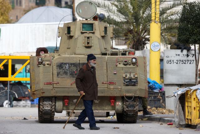 A Palestinian man walks past an Israeli armoured vehicle after Israel's security forces closed part of the H2 southern sector of the occupied West Bank city of Hebron, and announced a curfew as they search for weapons and Palestinians on their wanted list, on January 20, 2026. Following the 1995 Oslo Agreement and subsequent 1997 Hebron Agreement, Palestinian cities in the West Bank were placed under the exclusive jurisdiction of the Palestinian Authority, with the exception of Hebron, which was split into two sectors: H1 is controlled by the Palestinian Authority and H2 – which includes the Old City of Hebron – remaining under the military control of Israel. Most Palestinians live in the H2 sector. (Photo by HAZEM BADER / AFP)