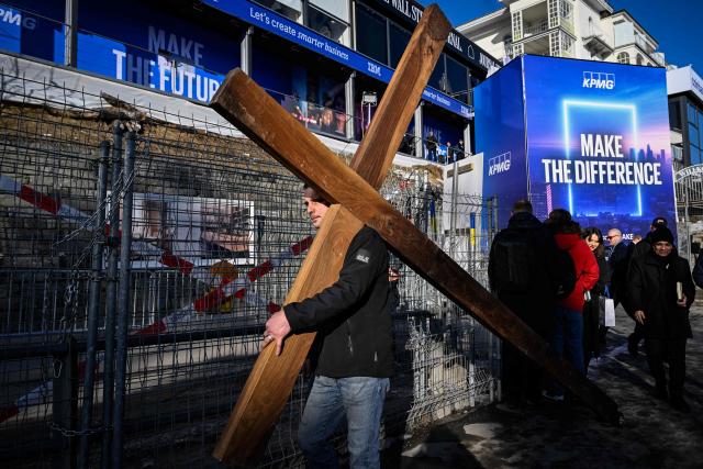 A man carries a large wooden cross through the streets of Davos on the sidelines of the World Economic Forum (WEF) annual meeting in Davos on January 20, 2026. The World Economic Forum takes place in Davos from January 19 to January 23, 2026. (Photo by INA FASSBENDER / AFP)