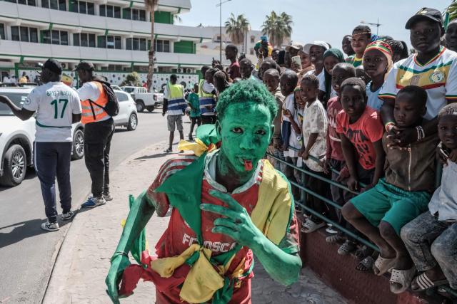A Senegalese football supporter, painted in green, gestures as he runs past other supporters waiting for the bus with the team on board to drive past during a trophy parade in the streets of Dakar on January 20, 2026 as they celebrate Senegal winning the Africa Cup of Nations (CAN) that was hosted in Morocco. Senegal won the Africa Cup of Nations in Rabat on January 18, 2026, Pape Gueye's extra-time winner sinking hosts Morocco 1-0 after a chaotic final that saw the eventual champions storm off the pitch late in the game. (Photo by GUY PETERSON / AFP)