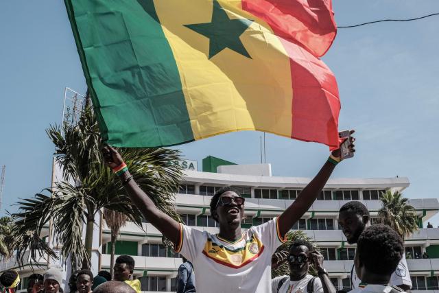 A Senegalese football supporter waves a Senegalese flag while waiting for the bus with the team on board to drive past during a trophy parade in the streets of Dakar on January 20, 2026 as they celebrate Senegal winning the Africa Cup of Nations (CAN) that was hosted in Morocco. Senegal won the Africa Cup of Nations in Rabat on January 18, 2026, Pape Gueye's extra-time winner sinking hosts Morocco 1-0 after a chaotic final that saw the eventual champions storm off the pitch late in the game. (Photo by GUY PETERSON / AFP)