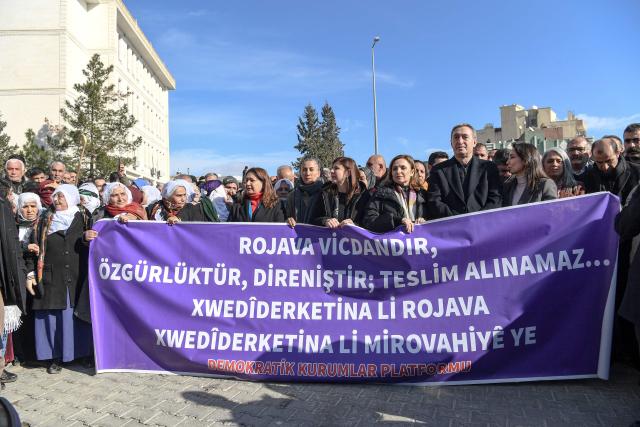 Co-leaders of pro-Kurdish Peoples Equality and Democracy Party (DEM Party) Tuncer Bakirhan (3rd R), Tulay Hatimogullari (2nd R) and supporters holds a banner reading "Rojava is conscience, freedom, resistance. It cannot be taken" during a rally against an offensive of Syrian government forces against Kurdish forces, near Nusaybin border gate in Mardin, on the Turkey-Syria border, on January 20, 2026. Clashes erupted on Turkey's border with Syria on between police and pro-Kurdish protesters angered by a Syrian military offensive targeting Kurds, an AFP correspondent said. The violence broke out in the border town of Nusaybin, just across from the northern Syrian town of Qamishli, at a protest called by the pro-Kurdish DEM, Turkey's third-largest party. (Photo by Ilyas AKENGIN / AFP)