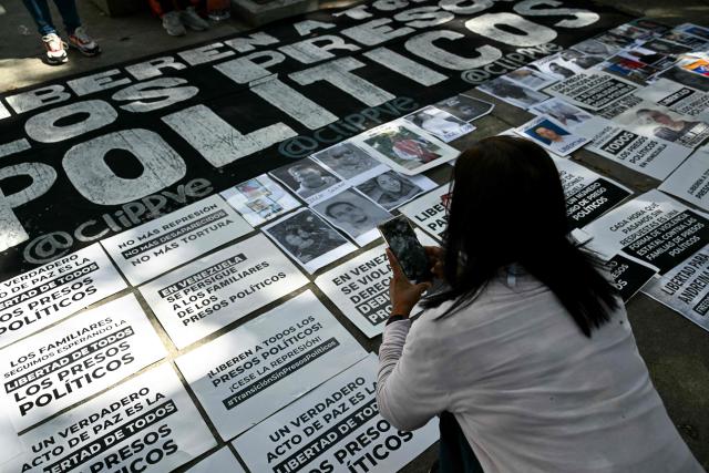 A woman takes pictures with her mobile phone as relatives of political prisoners protest displaying pictures and signs in front of the public prosecutor's office in Caracas on January 20, 2026. Dozens of journalists, government critics and activists have been freed in Venezuela since the US military deposed Nicolas Maduro this month. Rights group Foro Penal counts 90 political prisoner releases since January 8, while interim president Delcy Rodriguez says 406 people have been freed since December. Several prominent opposition figures, however, remain jailed despite US pressure (Photo by RONALDO SCHEMIDT / AFP)