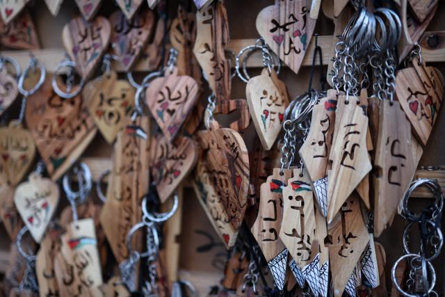 Wooden key rings carved with names (L) and the word Palestine (R), are displayed after being crafted in the shop in Ramallah, in the occupied West Bank, on January 20, 2026. (Photo by Zain JAAFAR / AFP)