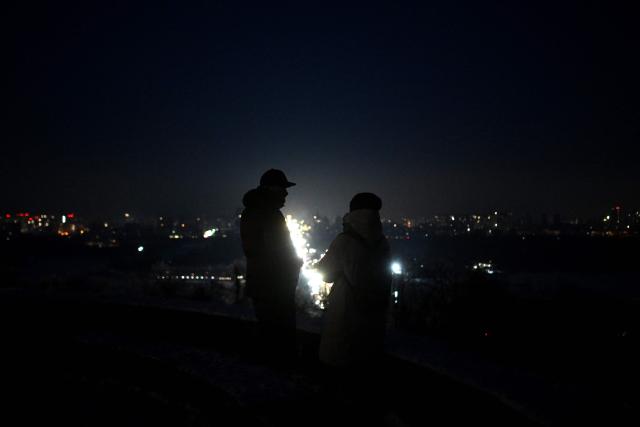 A couple stands at a viewing platform as cars drive along a road during a power outage in Kyiv on January 20, 2026, amid the Russian invasion of Ukraine. An overnight Russian bombardment left thousands of residential buildings in Kyiv without heating and water in -14C temperatures on January 20, 2026, when the Ukrainian capital was already scrambling to restore vital utilities destroyed in earlier attacks. (Photo by Sergei GAPON / AFP)