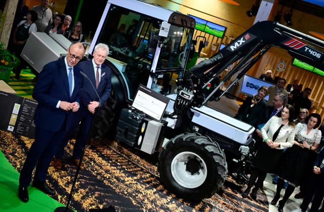 German Chancellor Friedrich Merz (L) stands next to German Minister for Agriculture Alois Rainer (2nd L) in front of an Onox1 electric tractor as he delivers a statement at the end of his tour at the "Gruene Woche" (Green Week) International Agriculture Fair in Berlin on January 20, 2026. The 100th edition of the Green Week, one of the world's leading events in the food, agriculture and horticulture sectors, will be running from January 16 to 25, 2026, and some 1600 exhibitors from over 50 countries are presenting their products and services. (Photo by John MACDOUGALL / AFP)