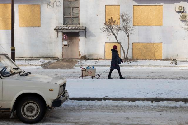 A woman pulls empty water bottles on a sled near a damaged residential building in Kramatorsk on January 20, 2026, amid the Russian invasion of Ukraine. (Photo by Tetiana DZHAFAROVA / AFP)