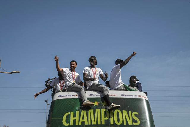 TOPSHOT - Senegal's Football Team players greet a crowd of supporters while riding on an open bus past supporters during a trophy parade in the streets of Dakar on January 20, 2026 as they celebrate Senegal winning the Africa Cup of Nations (CAN) that was hosted in Morocco. Senegal won the Africa Cup of Nations in Rabat on January 18, 2026, Pape Gueye's extra-time winner sinking hosts Morocco 1-0 after a chaotic final that saw the eventual champions storm off the pitch late in the game. (Photo by NICOLAS REMENE / AFP)
