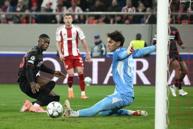 Olympiakos' Greek goalkeeper #88 Kostas Tzolakis makes a save in front of Bayer Leverkusen's Cameroonian forward #35 Christian Michel Kofane (L) during the during the UEFA Champions League, league phase day 7, football match between Olympiakos and Bayer Leverkusen at the Georgios Karaiskakis Stadium in Piraeus, near Athens, on January 20, 2026. (Photo by Angelos Tzortzinis / AFP)