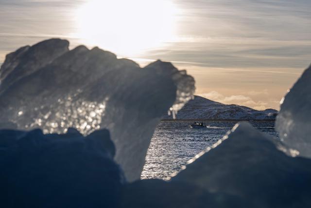 A boat passes through coastal waters, is pictured through ice blocks along the shoreline in Nuuk, Greenland, on January 20, 2026. (Photo by Jonathan NACKSTRAND / AFP)