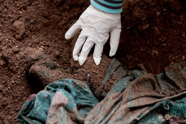 EDITORS NOTE: Graphic content / A member of the "Guerreros Buscadores" (Searching Warriors) touches an unearthed body during a search near a drug house in Tlajomulco de Zuniga, Jalisco state, Mexico on January 20, 2026. The Mexican collective "Guerreros Buscadores" went to an area near a drug house in Tlajomulco de Zuniga after receiving an anonymous tip that several bodies had recently been buried there, while the National Guard arrested one suspect. (Photo by Ulises RUIZ / AFP)