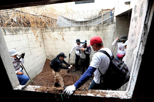 Members of the "Guerreros Buscadores" (Searching Warriors) collective dig up a body from a clandestine grave during a search at a drug house in Tlajomulco de Zuniga, Jalisco state, Mexico on January 20, 2026. The Mexican collective "Guerreros Buscadores" went to an area near a drug house in Tlajomulco de Zuniga after receiving an anonymous tip that several bodies had recently been buried there, while the National Guard arrested one suspect. (Photo by ULISES RUIZ / AFP)
