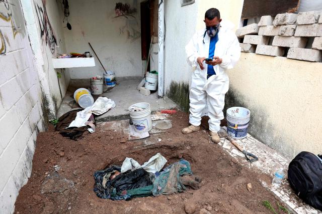 EDITORS NOTE: Graphic content / A member of the "Guerreros Buscadores" (Searching Warriors) collective works next to a body unearthed from a clandestine grave during a search at a drug house in Tlajomulco de Zuniga, Jalisco state, Mexico on January 20, 2026. The Mexican collective "Guerreros Buscadores" went to an area near a drug house in Tlajomulco de Zuniga after receiving an anonymous tip that several bodies had recently been buried there, while the National Guard arrested one suspect. (Photo by Ulises RUIZ / AFP)