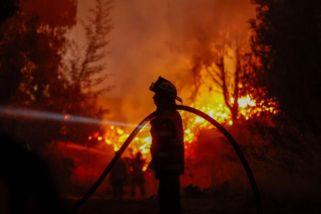 TOPSHOT - A firefighter carries a hose as he works to extinguish the burning vegetation during a wildfire in the town of Florida near the city of Concepción, Chile, on January 20, 2026. Residents of southern Chile, ravaged by four days of deadly wildfires, pleaded for help on January 20 from communities reduced to rubble, as smoke lingered and firefighters braced for the return of hot weather. (Photo by Raul BRAVO / AFP)