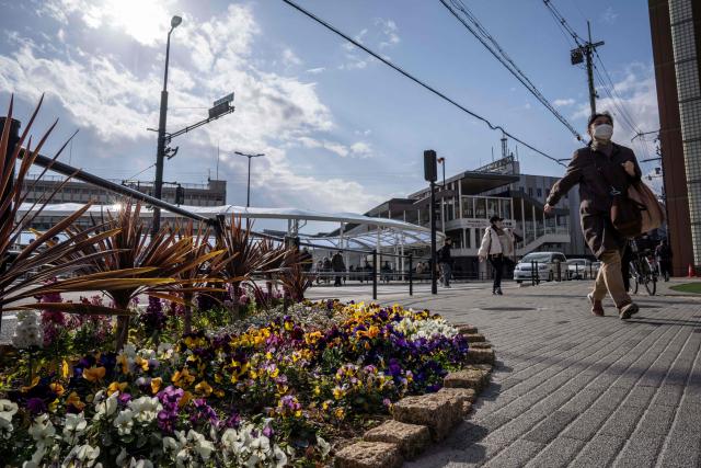 This photo taken on January 13, 2026 shows people walking past a flower bed set up as a memorial at the intersection in front of Kintetsu Yamato-Saidaiji Station where Japan's former prime minister Shinzo Abe was fatally shot while delivering an election campaign speech, in Nara, Nara prefecture. The gunman charged with killing Abe faces a verdict on January 21, 2026, more than three years after the broad-daylight assassination shocked the world. (Photo by Yuichi YAMAZAKI / AFP)