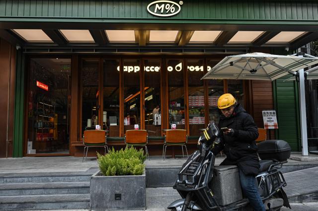 A delivery man rides past the first Colombian coffee brand Juan Valdez Café in Shanghai on January 21, 2026. (Photo by Jade GAO / AFP)