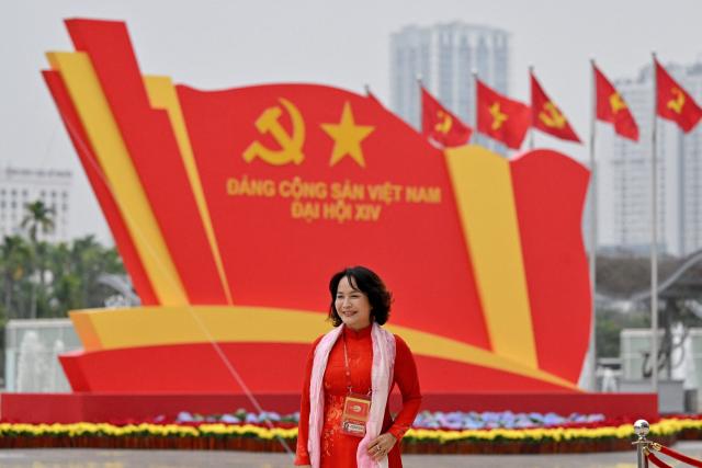 A delegate poses for a photo in front of a billboard for the 14th National Congress of the Communist Party of Vietnam at the National Convention Centre in Hanoi on January 21, 2026. (Photo by Nhac NGUYEN / AFP)