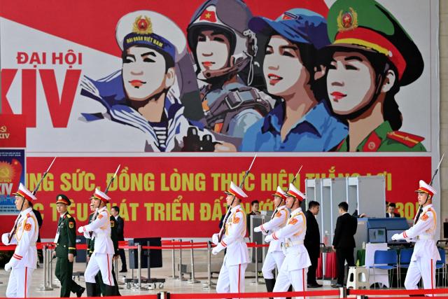 Honour guards walk past a billboard advertising the 14th National Congress of the Communist Party of Vietnam at the National Convention Centre in Hanoi on January 21, 2026. (Photo by Nhac NGUYEN / AFP)