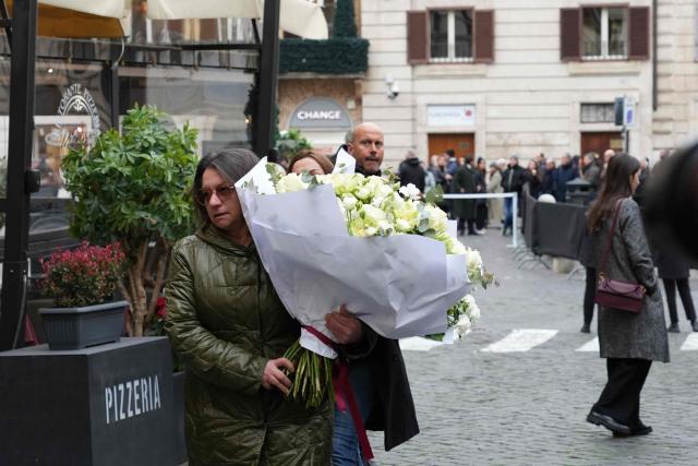 A woman holds a bouquet of white flowers as she arrives at  the PM23 exhibition site where late Italian fashion designer Valentino Garavani is lying in state before the funeral, in Rome on January 21, 2026. (Photo by Stefano Costantino / AFP)