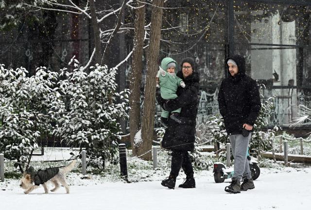 A pedestrian couple walks in winter clothes with a baby and a dog as snow falls on a snow-covered street in Skopje on January 21, 2026. (Photo by Robert ATANASOVSKI / AFP)