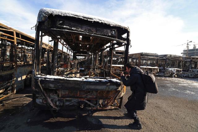 This photograph taken during a tour for foreign media shows a photographer taking pictures of the parked buses that were burnt at a depot during recent public protests, in Tehran on January 21, 2026. Demonstrations sparked in late December by anger over economic hardship exploded into protests widely seen as the biggest challenge to the Iranian leadership in years. Limited internet access briefly returned in Iran before dropping again, a monitor said January 18, 10 days into a communications blackout that rights groups said aimed to mask a protest crackdown that killed thousands. (Photo by ATTA KENARE / AFP)