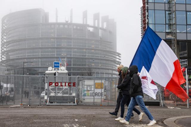French demonstrators with France's flag walk past a police barrier in front of the European Parliament building as they take part in a protest against the free trade agreement between the European Union and the Mercosur countries, on the day of a vote on a referral to the courts, in Strasbourg on January 21, 2026. The European Union's parliament voted on Janaury 21, 2026, to refer a freshly signed trade deal with South American bloc Mercosur to the EU's top court, casting a veil of legal uncertainty over the accord. (Photo by Romeo BOETZLE / AFP)