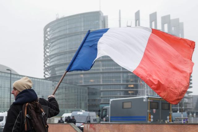 A demonstrator holds a French flag with the EU Parliament building in the background as farmers protest against the free trade agreement between the European Union and the Mercosur countries, on the day of a vote on a referral to the courts, in Strasbourg on January 21, 2026. The European Union's parliament voted on Janaury 21, 2026, to refer a freshly signed trade deal with South American bloc Mercosur to the EU's top court, casting a veil of legal uncertainty over the accord. (Photo by Romeo BOETZLE / AFP)