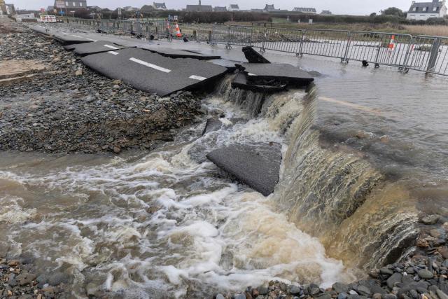 This photograph shows water flowing over a road collapsed due to a flood, in Pouldreuzic, western France on January 21, 2026. Finistиre and Morbihan departments of western France are on orange alert on January 21, 2026, for “rain and flooding”. (Photo by Fred TANNEAU / AFP)