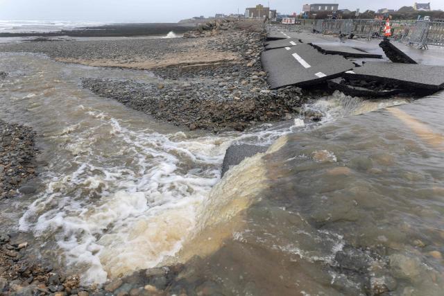 This photograph shows water flowing over a road collapsed due to a flood, in Pouldreuzic, western France on January 21, 2026. Finistиre and Morbihan departments of western France are on orange alert on January 21, 2026, for “rain and flooding”. (Photo by Fred TANNEAU / AFP)