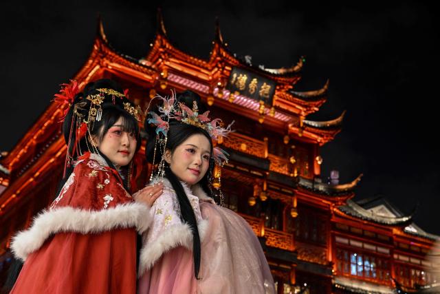 TOPSHOT - Women wearing traditional costumes pose for photographs at Yu Garden in Shanghai on January 21, 2026. (Photo by Hector RETAMAL / AFP)