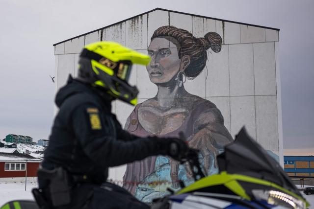 A police officer rides a snowmobile past a large mural depicting a woman and a polar bear on the side of an apartment building in Nuuk, Greenland, on January 21, 2026. (Photo by Jonathan NACKSTRAND / AFP)
