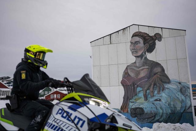 A police officer rides a snowmobile past a large mural depicting a woman and a polar bear on the side of an apartment building in Nuuk, Greenland, on January 21, 2026. (Photo by Jonathan NACKSTRAND / AFP)