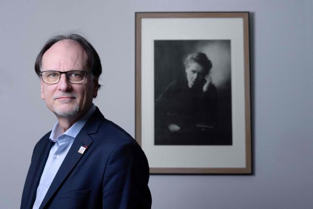 French pharmacist, biologist and Director of Institut Curie's Research Center Alain Puisieux, poses for photographs in front of a picture of French physicist and chemist Marie Curie, during a portrait session in his office, in Paris, on January 21, 2026. (Photo by JOEL SAGET / AFP)