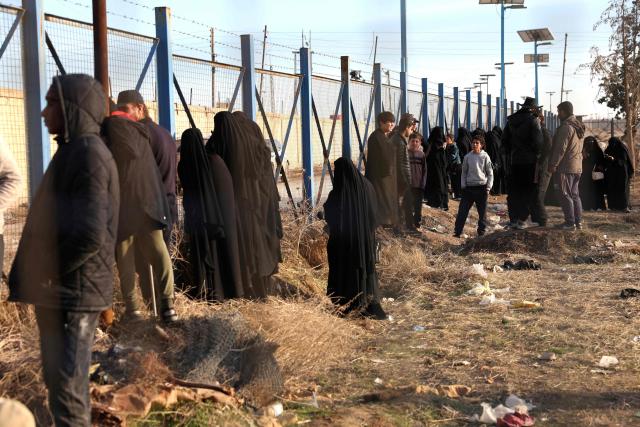 Relatives of suspected Islamic State jihadists, stand behind a fence in Al-Hol camp in the desert region of Syria's Hasakeh province on January 21, 2026. Syria's army entered the vast Al-Hol camp that houses relatives of suspected Islamic State jihadists after Kurdish forces withdrew from the site, said an AFP journalist at the scene. The camp in a desert region of Hasakeh province holds around 24,000 people, including some 6,200 women and children from around 40 nationalities. (Photo by OMAR HAJ KADOUR / AFP)