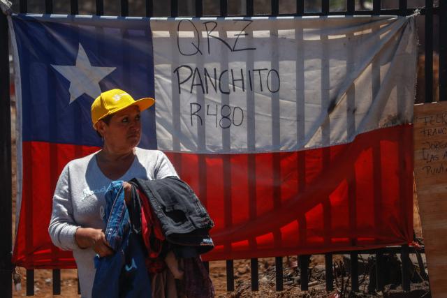 Felicia Lara poses at the entrance of her house, which was completely destroyed and is now decorated with a Chilean national flag, after the devastating forest fires that ravaged the area on January 3, in Punta de Parra, near Concepcion, Chile, on January 21, 2026. Police in south-central Chile have arrested a man on suspicion of starting one of the recent wildfires that killed 20 people and razed entire neighborhoods, the government said on January 21. (Photo by Raul BRAVO / AFP)