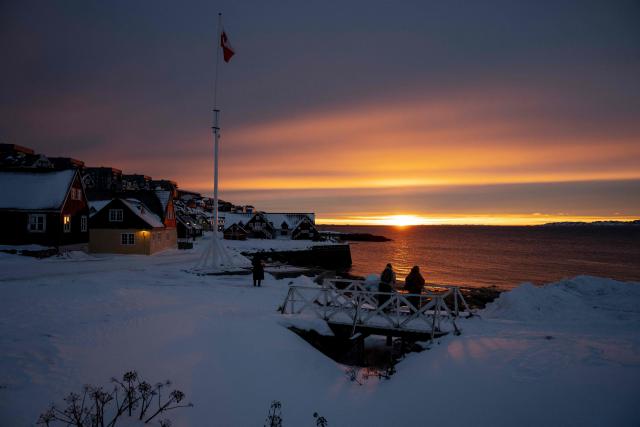 People watch from a bridge over the water at the sunset as a flag hangs and the city is seen on the background in Nuuk, Greenland, on January 21, 2026. (Photo by Mads Claus Rasmussen / Ritzau Scanpix / AFP) / Denmark OUT