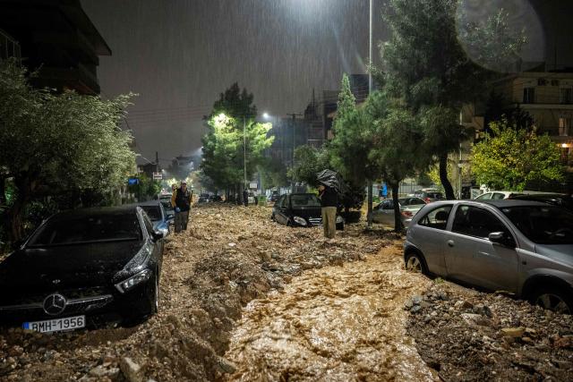 Peolple stand in a flooded street covered with rubbles after a heavy rainfalls in Ano Glyfada, southern of Athens, on January 21, 2026. (Photo by Aris MESSINIS / AFP)