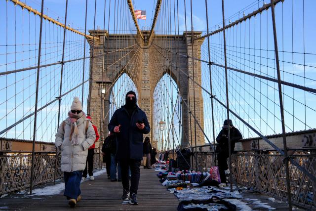 People brace the cold temperatures while walking on the Brooklyn Bridge in the Manhattan borough of New York City on January 21, 2026. Bringing icy temperatures, Winter Storm Fern will slam a massive stretch of the United States this week, with more than 175 million people facing the prospect of heavy snowfall, power outages and travel disruption. Forecasters warned it could be 2,000 miles (3,219 kilometers) long -- well over half the length of the continental US. (Photo by CHARLY TRIBALLEAU / AFP)