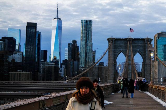 People brace the cold temperatures while walking on the Brooklyn Bridge in the Manhattan borough of New York City on January 21, 2026. Bringing icy temperatures, Winter Storm Fern will slam a massive stretch of the United States this week, with more than 175 million people facing the prospect of heavy snowfall, power outages and travel disruption. Forecasters warned it could be 2,000 miles (3,219 kilometers) long, well over half the length of the continental US. (Photo by CHARLY TRIBALLEAU / AFP)