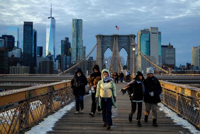 People brace the cold temperatures while walking on the Brooklyn Bridge in the Manhattan borough of New York City on January 21, 2026. Bringing icy temperatures, Winter Storm Fern will slam a massive stretch of the United States this week, with more than 175 million people facing the prospect of heavy snowfall, power outages and travel disruption. Forecasters warned it could be 2,000 miles (3,219 kilometers) long -- well over half the length of the continental US. (Photo by CHARLY TRIBALLEAU / AFP)
